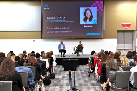 Conference room with two people on stage. Session sponsored by Deloitte