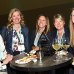 Five women around a high top table with snacks and drinks.