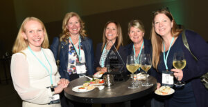 Five women around a high top table with snacks and drinks.